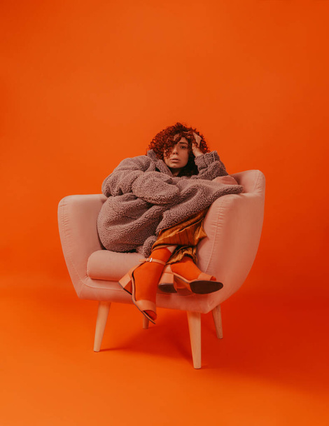 Руда кучерява дівчина в студії на помаранчевому фоні в стильному одязі
 - Фото, зображення