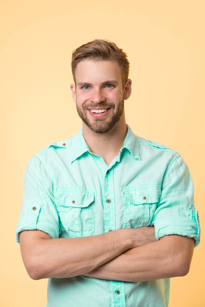 Cheerful consultant. Man smiling face posing confidently with folded arms yellow background. Man shop consultant looks cheerful confident and hospitable. Guy with bristle glad to help you in shop - Photo, Image