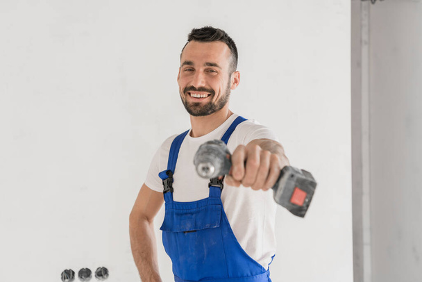 Reparador alegre apunta con un taladro a la cámara - Foto, Imagen