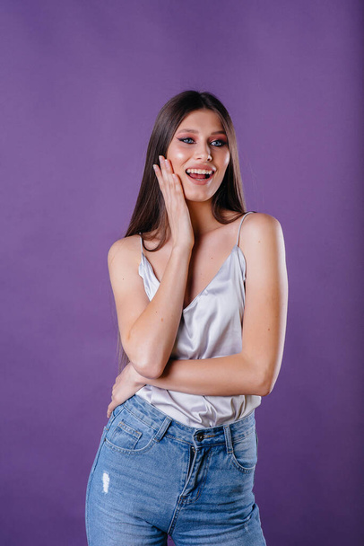 A young beautiful girl shows emotions and smiles in the Studio on a purple background. Girls for advertising - Valokuva, kuva