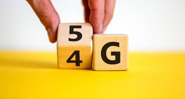Time to 5G. Male hand turns wooden block and changes sign 4G to 5G. Technology, network, communication concept. Beautiful yellow table. White background, copy space. - Фото, изображение