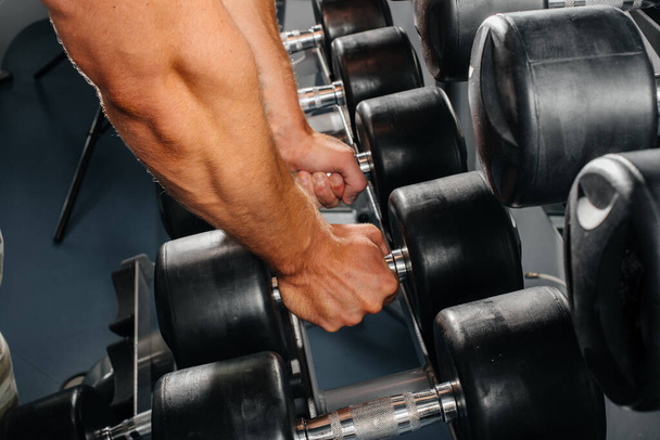 An athlete takes dumbbells from racks in the gym, close-up. Fitness, bodybuilding - Foto, immagini