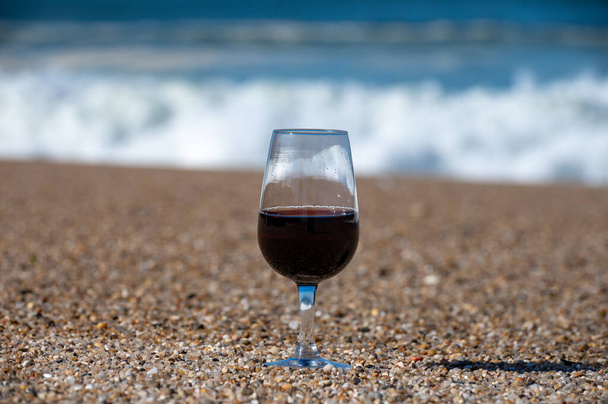 Dégustation de différents rubis de dessert fortifié, vins de porto tawny en verre sur une plage de sable avec vue sur les vagues de l'océan Atlantique près de Vila Nova de Gaia et la ville de Porto, Portugal - Photo, image