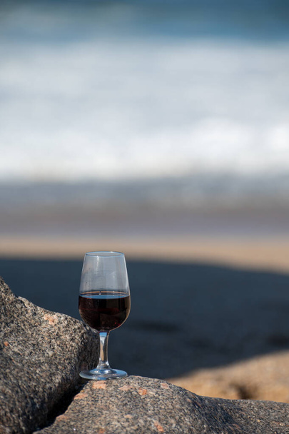 Degustacja różnych ufortyfikowanych win z rubinu, tawny port w szkle na piaszczystej plaży z widokiem na fale Oceanu Atlantyckiego w pobliżu Vila Nova de Gaia i miasta Porto, Portugalia - Zdjęcie, obraz