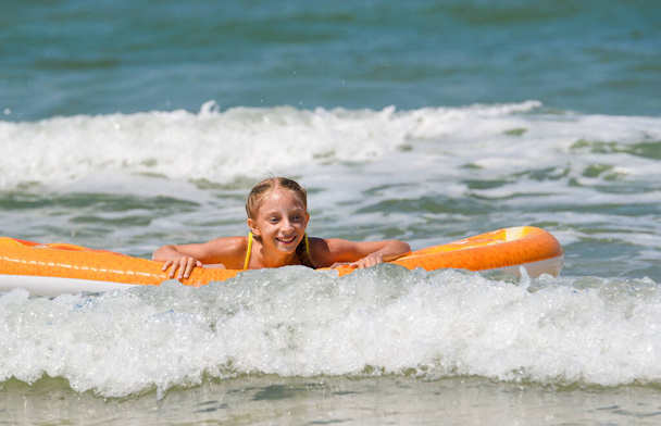 vrolijk meisje drijft op de zee golven op een opblaasbare matras - Foto, afbeelding