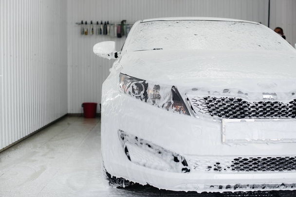 Lavado moderno con espuma y agua de alta presión de un coche blanco. Lavado de coches - Foto, Imagen