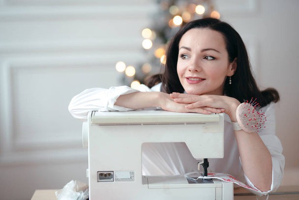 Gorgeous Caucasian seamstress girl with a pin-cushion on her wrist and sewing machine. Sewing concept - Photo, Image