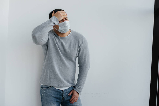 A young man stands on a gray background wearing a mask during a quarantine with free space. Quarantine in the mask - Foto, imagen