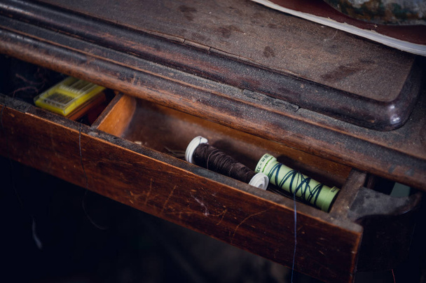 In un cassetto aperto di un vecchio tavolo di legno polveroso sono fili e aghi da cucito - Foto, immagini