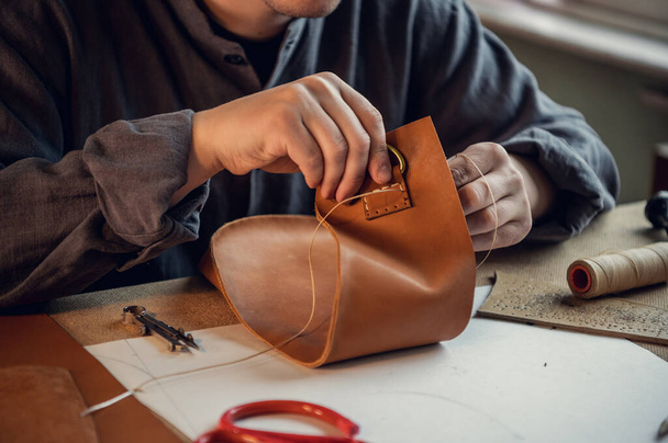 Ein erfahrener Gerber näht einen Verschluss für ein Lederprodukt mit Nähten - Foto, Bild