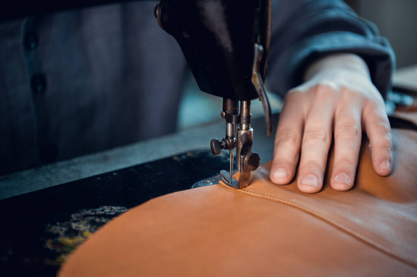 The process of stitching two pieces of genuine leather by a shoemaker on a special old-school sewing machine. Stitches of thread and the hand of the master - Foto, immagini