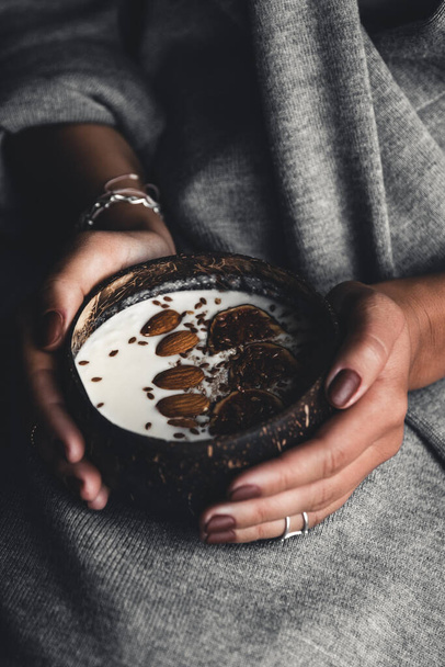A coconut bowl in the hands of a girl with yogurt and figs. - Foto, afbeelding