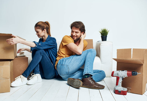 man and woman sitting on the floor with their backs to each other renovation work moving a flower in a pot - Photo, Image