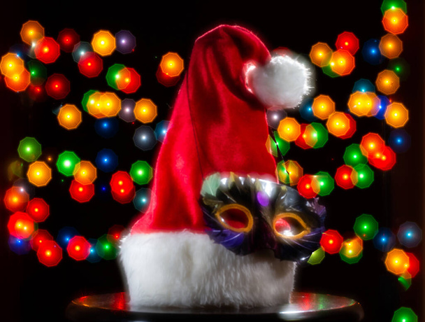 Chapeau de Père Noël avec masque de carnaval dans un accent doux sur le fond de lumières colorées. - Photo, image