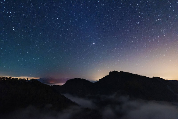 A beautiful starry night in the mountains on top with beautiful scenery and fog. - Photo, image