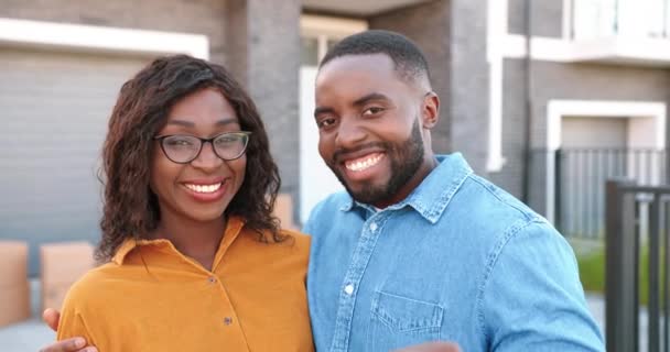 Retrato de feliz alegre jovem casal afro-americano sorrindo para a câmera e mostrando para as teclas de câmera de nova casa. Ao ar livre. A comprar imóveis. Movendo-se em conceito. Caixas de cartão em segundo plano. - Filmagem, Vídeo
