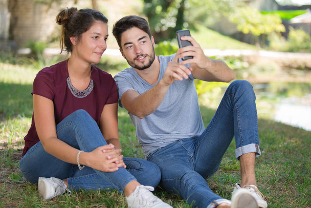 Couple sat on grass taking a selfie - Foto, imagen