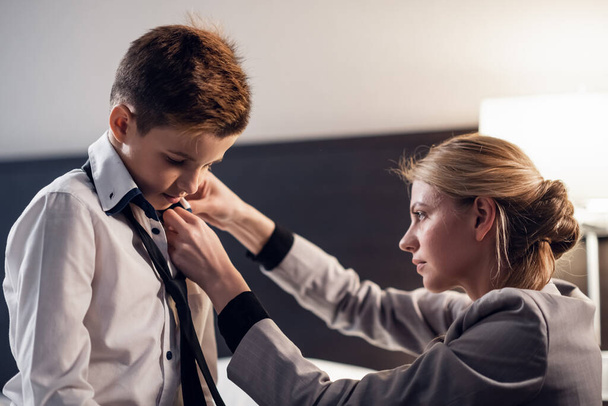 A close up picture of a mother fixing her little sons tie in th - Φωτογραφία, εικόνα