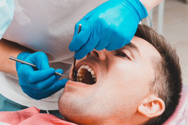 Zahnklinik, der Patient sitzt mit weit geöffnetem Mund im Zahnarztstuhl, der Zahnarzt beurteilt den Zustand der Zähne und stellt eine Diagnose. 2020 - Foto, Bild