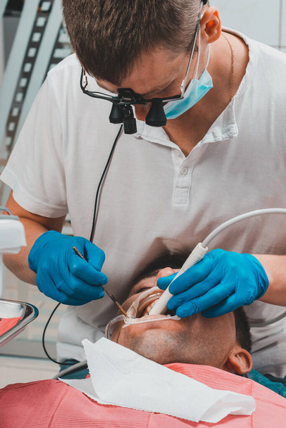 Dentysta w klinice, zabieg usuwania tatuaży, dentysta w lornetce usuwa tatuaż w ustach pacjentki.2020 - Zdjęcie, obraz