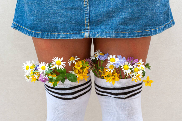 female legs with fresh flowers in stockings. A young hipster girl with flowers from white stockings and jeans skirt - 写真・画像