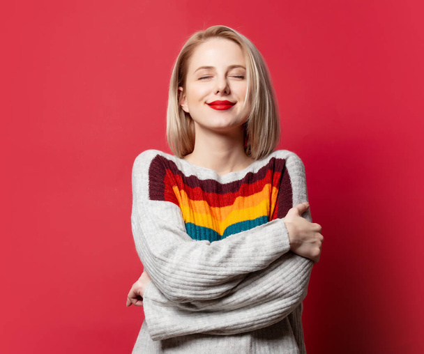 Piękna blondynka w swetrze na czerwonym tle  - Zdjęcie, obraz