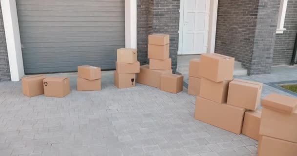 Kartonnen dozen op de grond in de tuin van een vrijstaand huis in een buitenwijk. Verhuizen in concept. Afwikkeling. Onroerend goed kopen. Ik ben aan het wennen. Pakketten. - Video