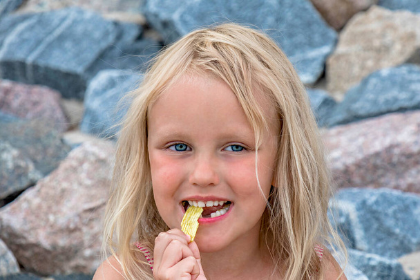 A 5-year-old blonde girl with a lost milk tooth eats chips - Photo, Image