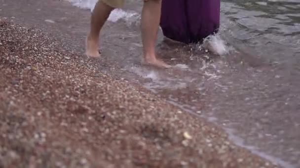 bosé nohy muže a ženy kráčející bok po boku na oblázkové pláži ve vodě - Záběry, video