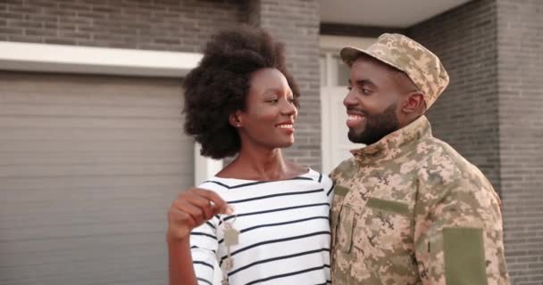Portrait de jeunes afro-américains mariés couple de soldats de l'armée debout dans des câlins en plein air à la maison, souriant et montrant la clé de la caméra. Officier en uniforme avec femme emménageant dans une nouvelle maison. Immobilier - Séquence, vidéo
