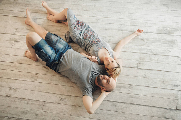 Een man met een baard en een blond meisje zitten op de vloer tussen de kussens. Gitaar, emoties, liefde. Liefdesverhaal. - Foto, afbeelding
