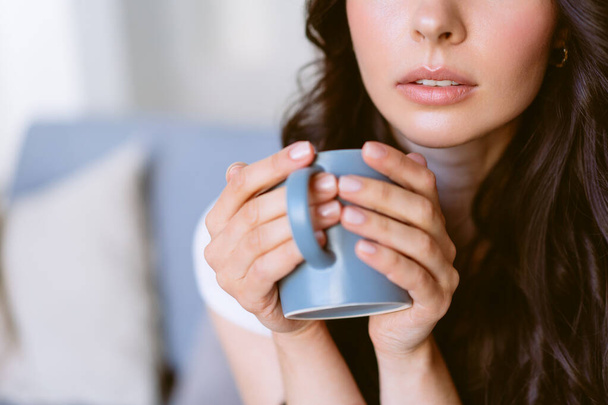 Genç, mutlu bir kadın çay içiyor ve rüyasında parlak bir dairede koltukta oturuyor.. - Fotoğraf, Görsel