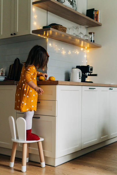 Caucasian girl peeling tangerines on kitchen counter. Healthy child diet. Immune boosting with vitamin c - Fotó, kép