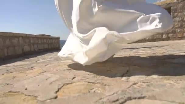 Morsian juoksee kivilaituria pitkin sulhasen luo, hänen mekkonsa hame lepattaa tuulessa - Materiaali, video