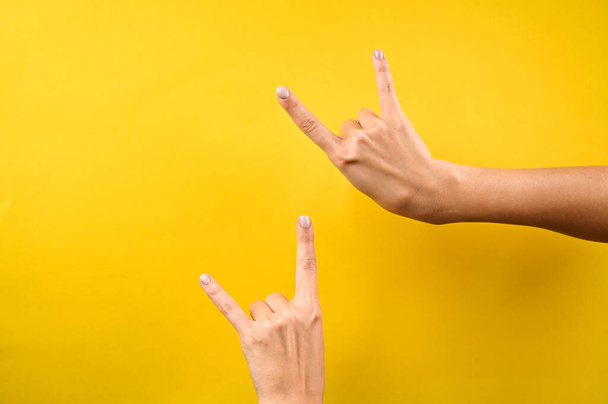 Woman's hand shows rock and roll hand signs isolated on yellow background. Horns sign. High quality photo - Photo, Image