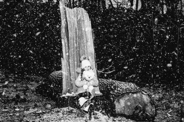 Menina engraçada na floresta de inverno nevado Ano Novo brinca com um urso branco de brinquedo. Retrato de inverno de uma criança. Retrato preto e branco. - Foto, Imagem