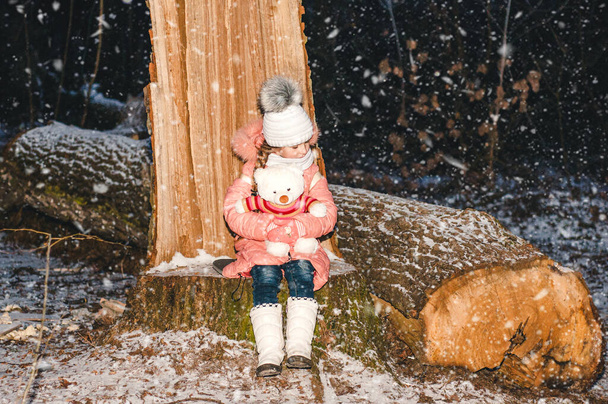 Lustiges kleines Mädchen im schneebedeckten Neujahrswald spielt mit einem weißen Bären. Winterporträt eines Kindes. - Foto, Bild