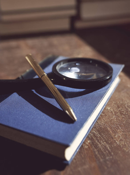 Vanha sininen kirja suurennuslasi ja kynä päällä, puinen pöytä - Valokuva, kuva