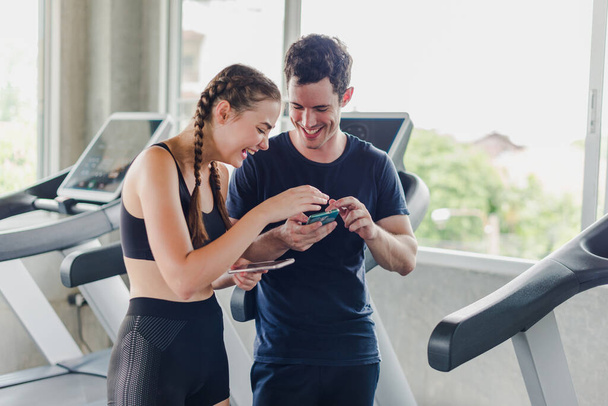 Couples exercise at the gym. Couple having fun playing with smartphones Near the exercise machine. - Фото, изображение
