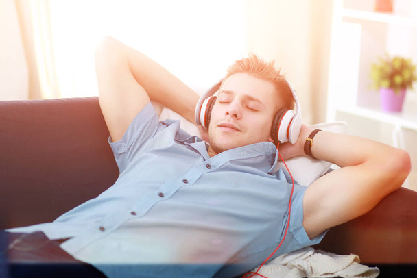 A young handsome man on the couch listening to music - Фото, изображение