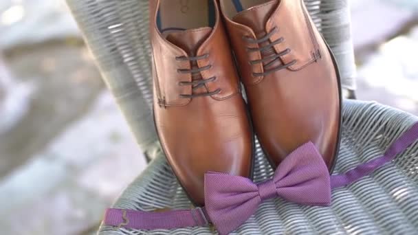 新郎の弓のネクタイは革の靴の近くにありますウィッカーチェアに立って準備をしながら - 映像、動画