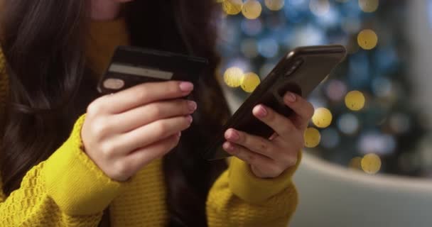 Lähikuva laukaus naisten käsissä pitämällä luottokorttia ja kirjoittamalla älypuhelin ostaa verkossa sisätiloissa. Nuori nainen sormet käyttäen matkapuhelin ostoksia internetissä lomakaudella. Ostokset käsite - Materiaali, video