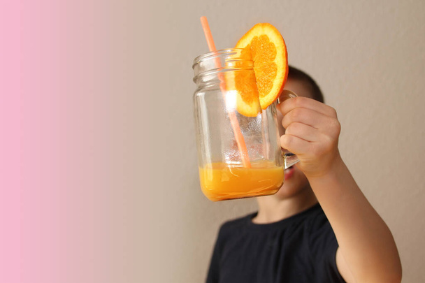 cheerful kid, boy, holds a glass jar in his hand with orange juice from orange or lemon, the concept of a healthy diet, vitamins, lifestyle - Foto, immagini