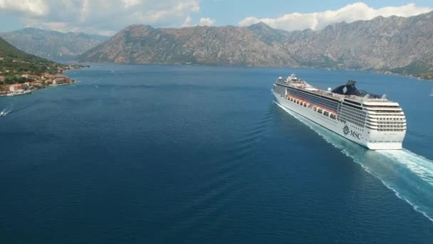 Het cruiseschip vaart langs de baai van Kotor, daarachter liggen prachtige bergen, kiezelstenen zijn zichtbaar in het heldere water, vanuit de lucht gezien - Video