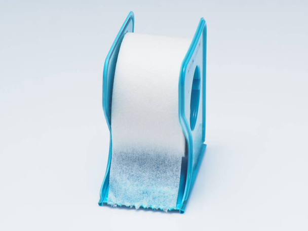 Witte chirurgische tape op een blauwe dispenser, close-up schot op witte geïsoleerde achtergrond - Foto, afbeelding