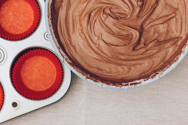 Pâte à cacao pour cupcakes, moules en papier rouge et plaque de cuisson en métal sur nappe. Préparation du processus de cuisson. Vue du dessus. - Photo, image