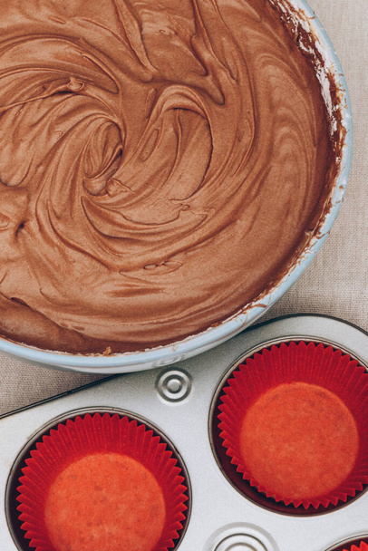 Pâte à cacao pour cupcakes, moules en papier rouge et plaque de cuisson en métal sur nappe. Préparation du processus de cuisson. Vue du dessus. - Photo, image