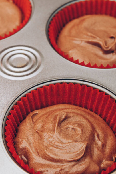 Pâte à cacao pour cupcakes dans des moules en papier rouge dans une plaque de cuisson en métal close-up. Préparation du processus de cuisson. - Photo, image