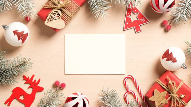 White paper card with red handmade Christmas decorations, gift boxes, candy canes on beige background. Flat lay, top view, copy space. Christmas card mockup. - Fotó, kép