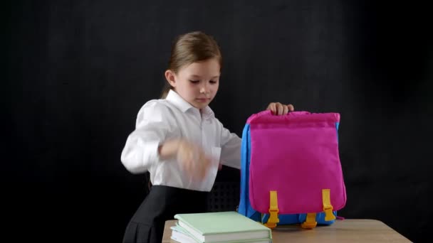 Petite écolière mettant des manuels dans son sac à dos en classe à la fin de la leçon - Séquence, vidéo